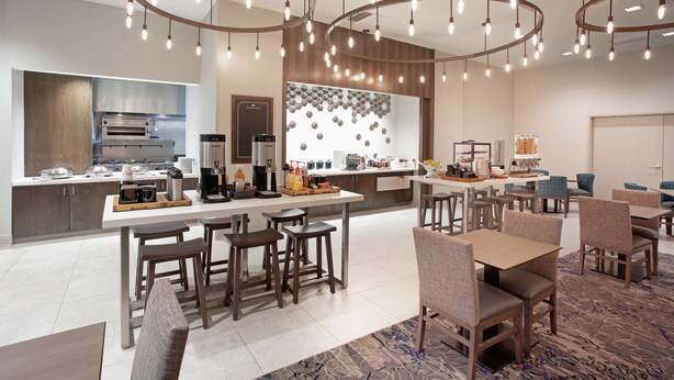 A modern hotel lobby with a central kitchen area, seating arrangements, and a patterned wall.