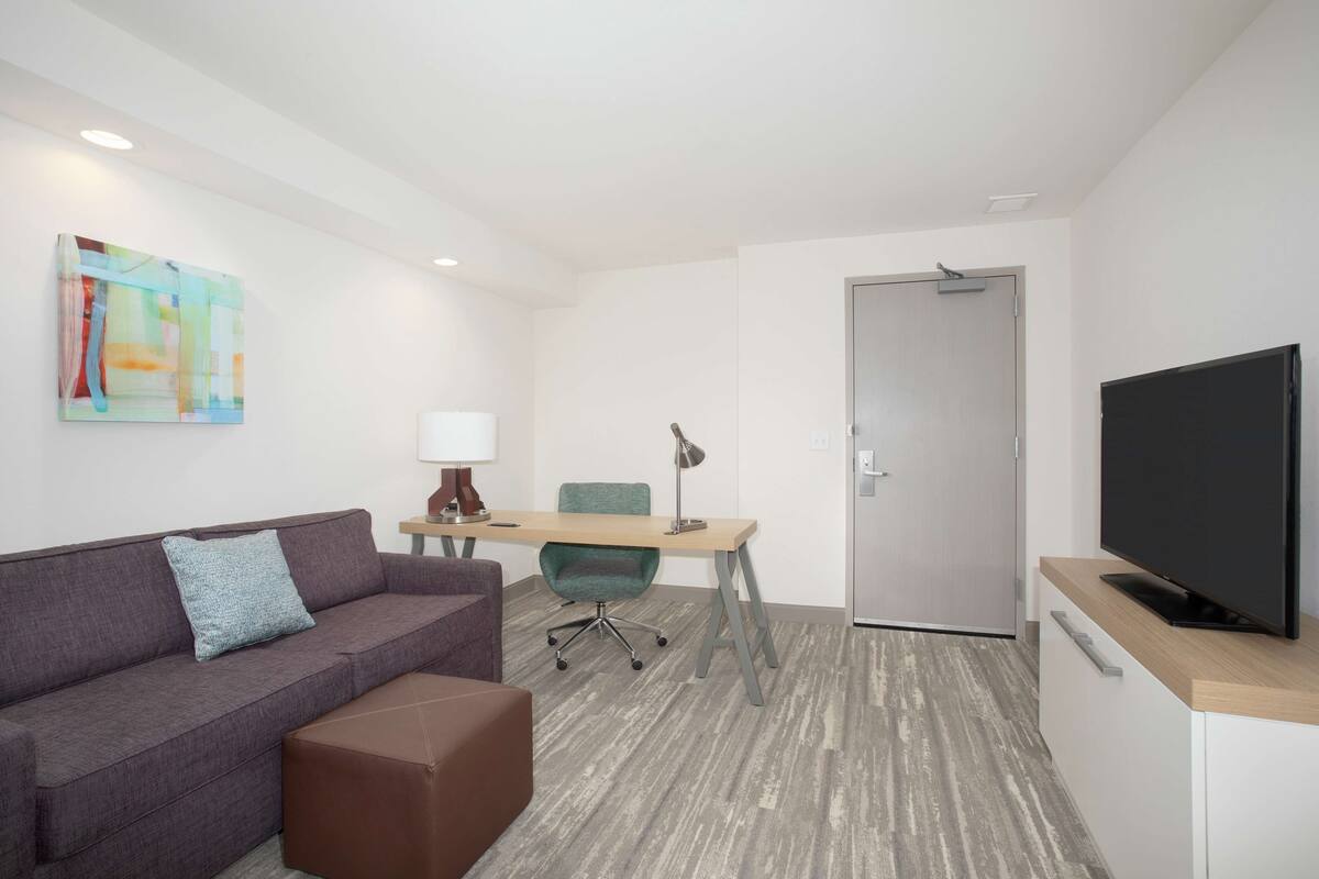 Una habitación de hotel moderna con sofá, escritorio, silla, televisión y puerta.