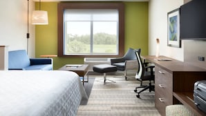 Quarto de hotel com cama, escrivaninha, cadeira, abajur e janela com vista para o verde.