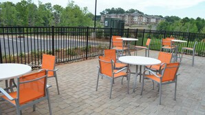 An outdoor seating area with tables and chairs, a paved walkway, and a fence.