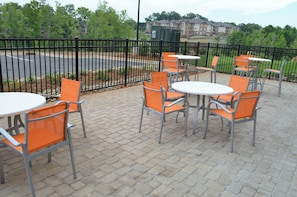 An outdoor seating area with tables and chairs, a paved walkway, and a fence.