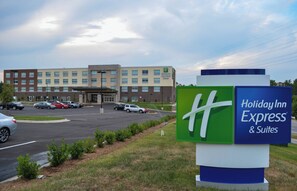 A Holiday Inn Express & Suites hotel with a parking lot and a large building in the background. - Holiday Inn Express & Suites Raleigh Airport - Brier Creek by IHG (Raleigh)
