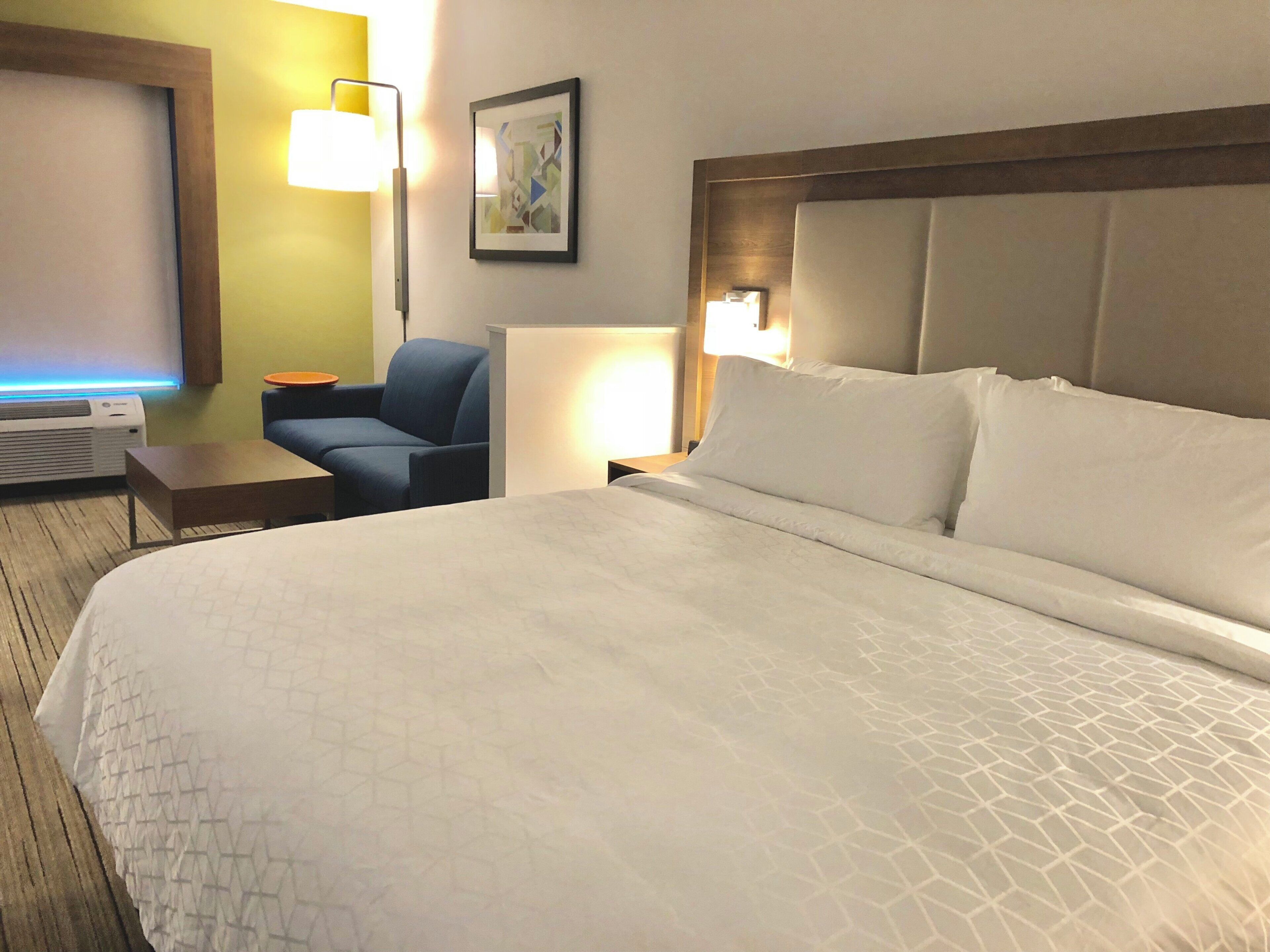 Ein Hotelzimmer mit einem großen Bett, einem Schreibtisch, einem Sessel, einer Lampe und einem Bild an der Wand.
