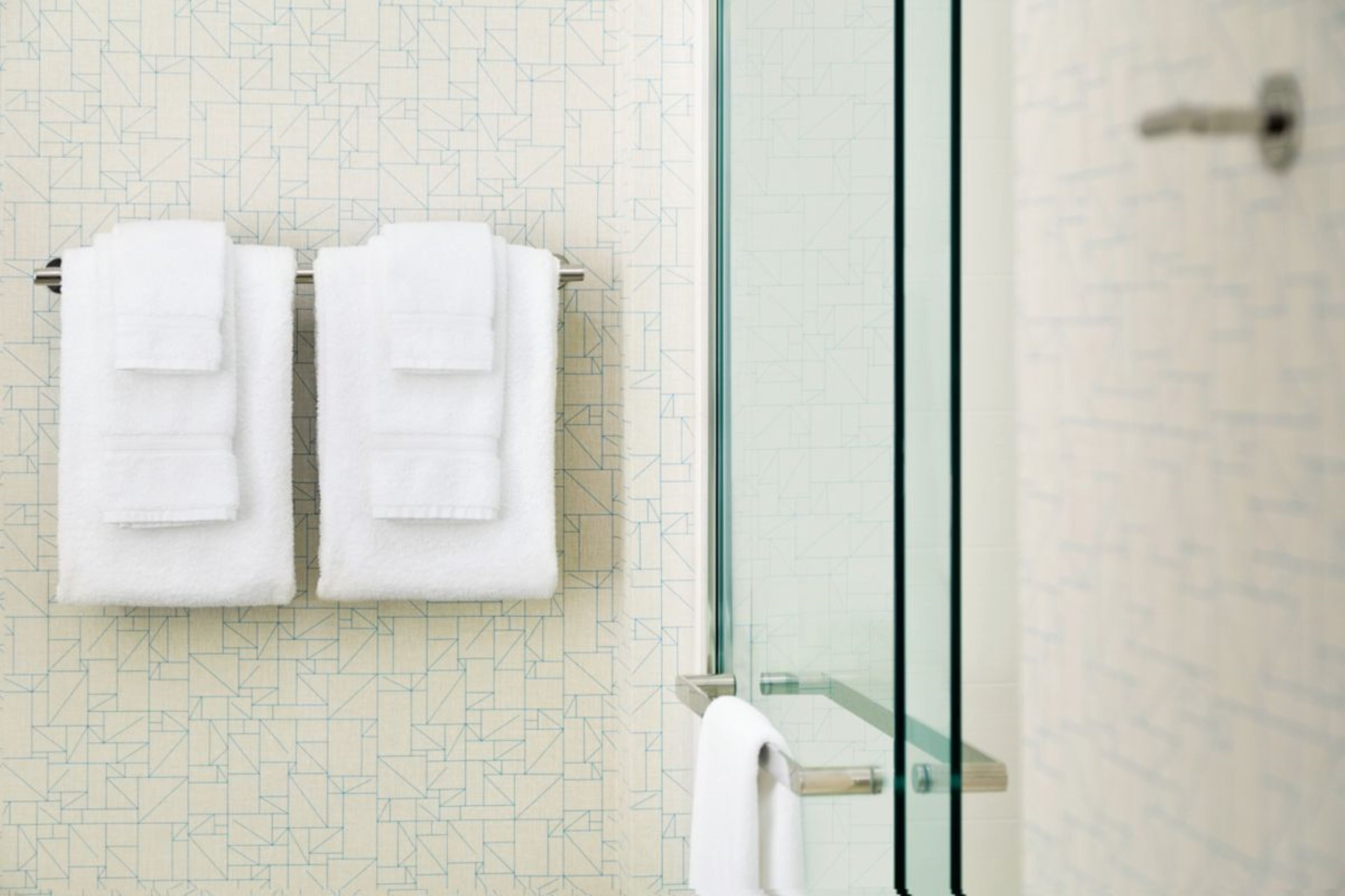 Un baño con pared estampada, cabina de ducha de cristal y dos toallas blancas colgadas en un perchero.