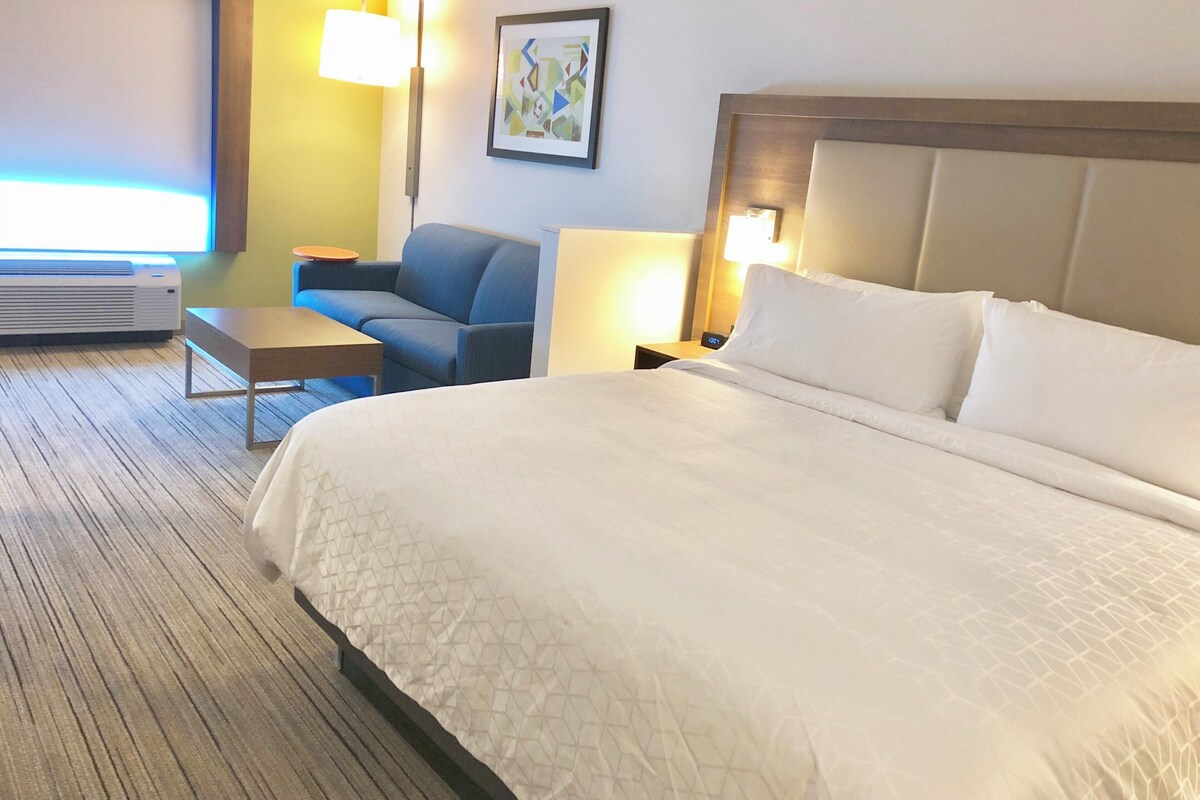 A hotel room with a large bed, a sofa, a small table, a lamp, and a painting on the wall.
