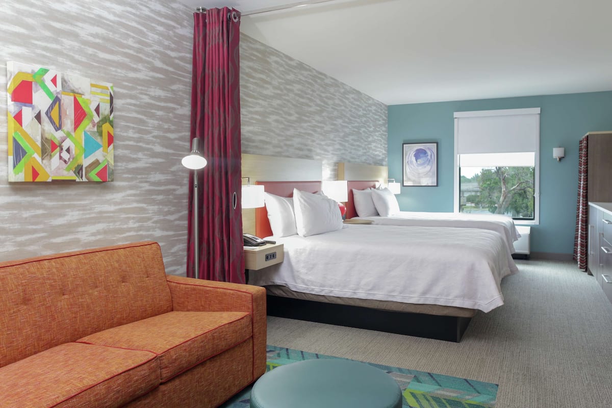 A hotel room with a bed, a sofa, a nightstand, a lamp, and a window with a view.