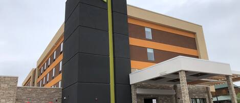 A hotel with a prominent black and beige facade, a vertical green stripe, and a sign reading "HOME 2 Suites by Hilton."