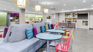 A modern lounge area with a grey sofa, colorful cushions, and a variety of seating options including red chairs and a table. - Home2 Suites by Hilton Fort Collins (Fort Collins)