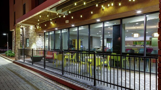 A modern building with a brick facade, large glass windows, and outdoor seating with yellow chairs. - Home2 Suites by Hilton Fort Collins (Fort Collins)