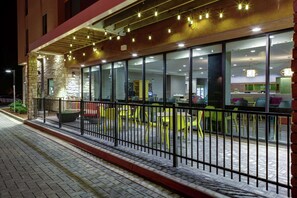 A modern building with a brick facade, large glass windows, and outdoor seating with yellow chairs. - Home2 Suites by Hilton Fort Collins (Fort Collins)