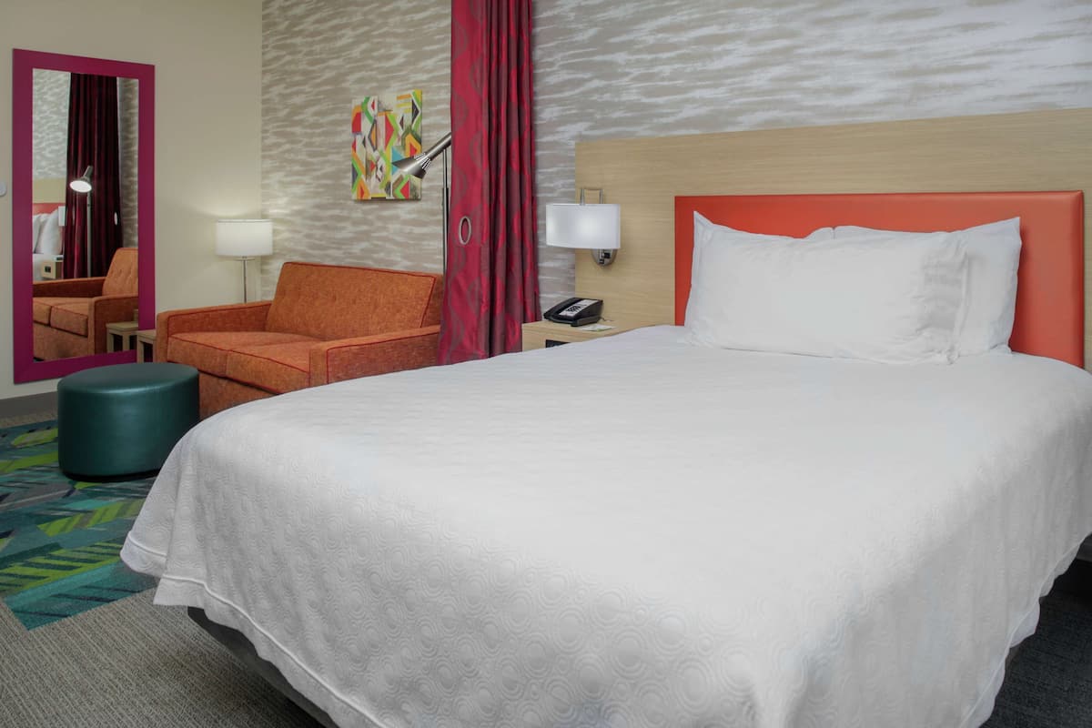 A hotel room with a large bed, a chair, a desk, and a mirror.