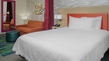 A hotel room with a large bed, a chair, a desk, and a mirror.
