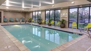 An indoor swimming pool with clear water, yellow chairs, and potted plants. - Home2 Suites by Hilton Fort Collins (Fort Collins)