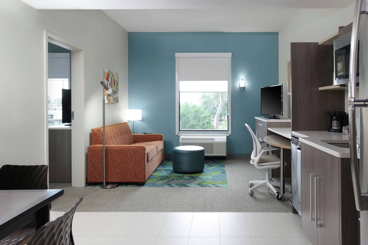 A modern kitchen with a built-in microwave, a coffee maker, and a refrigerator. There is a window with a view of trees outside.