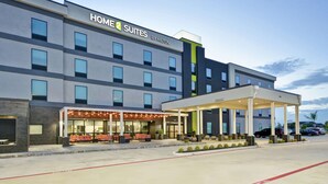 Un hotel con fachada moderna, un área de estar techada al aire libre y un estacionamiento.