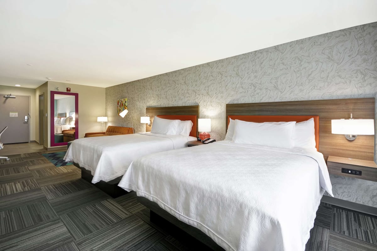 Habitación de hotel con dos camas, una puerta, un espejo y suelo alfombrado.