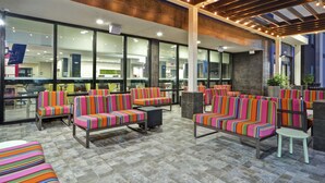 Un área de estar al aire libre con sofás y sillones a rayas, piso de baldosas y vistas del interior del hotel a través de amplias ventanas de vidrio.