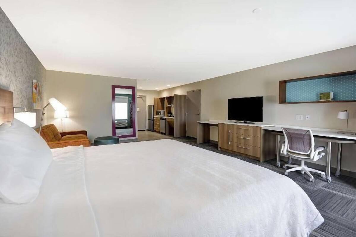 Una habitación de hotel con una cama grande, un escritorio, una silla, un televisor y una kitchenette.