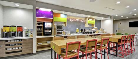 A modern cafe with a long wooden table and red chairs, a coffee machine, and a sign that reads "inspired table."