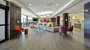 Un vestíbulo amplio con diseño moderno, que incluye una zona de estar con sofás y sillones, un mostrador de recepción y una cocina al fondo.