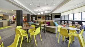 Un espacio interior moderno con sillas y mesas amarillas, un sofá con cojines de colores y una zona de cocina al fondo.