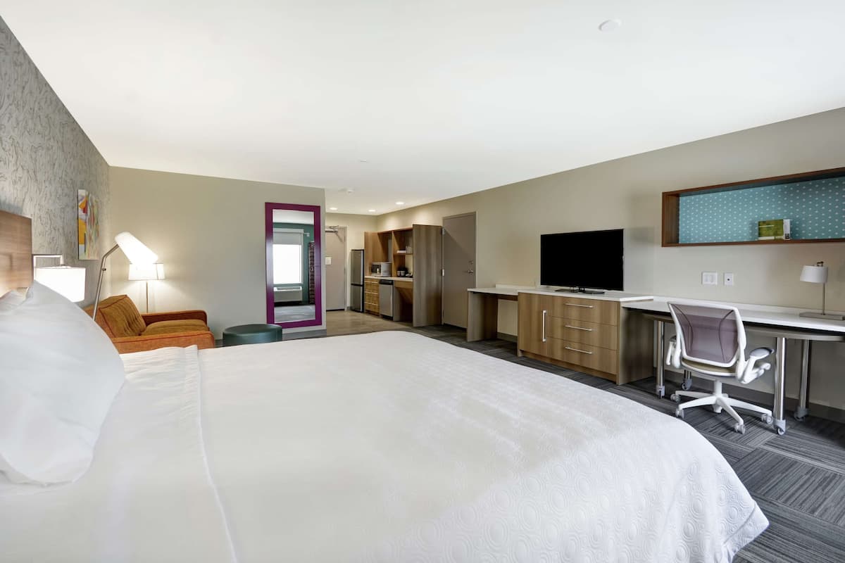 Una habitación de hotel con una cama grande, un escritorio, una silla, un televisor y una kitchenette.