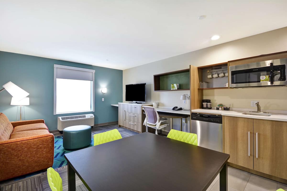 Habitación de hotel moderna con comedor, kitchenette y un ventanal que proporciona luz natural.