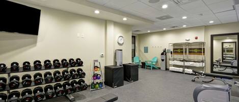 A gym with weightlifting equipment, cardio machines, and a wall-mounted TV.