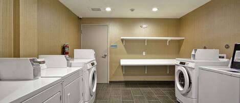 A laundry facility with multiple washing machines and dryers, a bench, and a fire extinguisher.