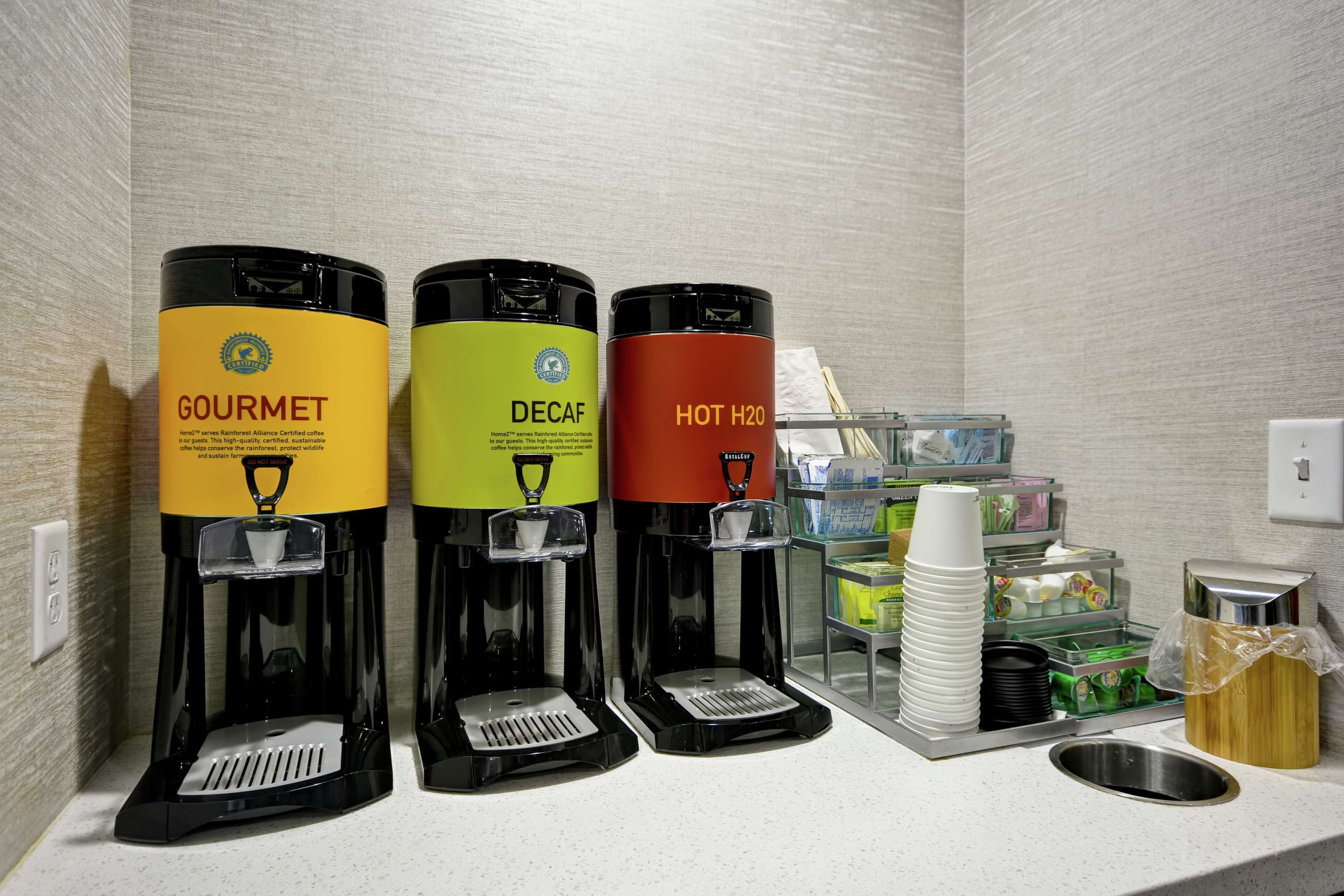 A coffee station with three dispensers labeled 'GOURMET,' 'DECAF,' and 'HOT H2O.'