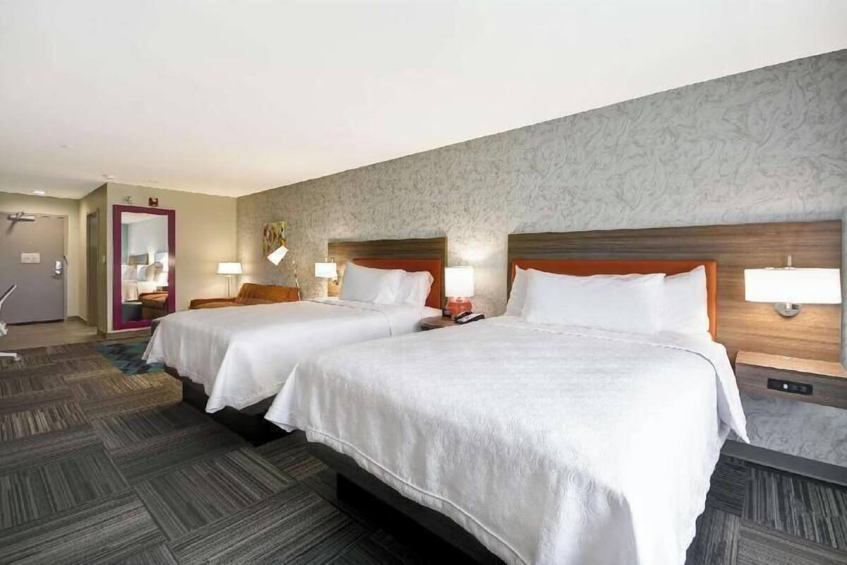 Habitación de hotel con dos camas, un espejo, una puerta y suelo alfombrado.