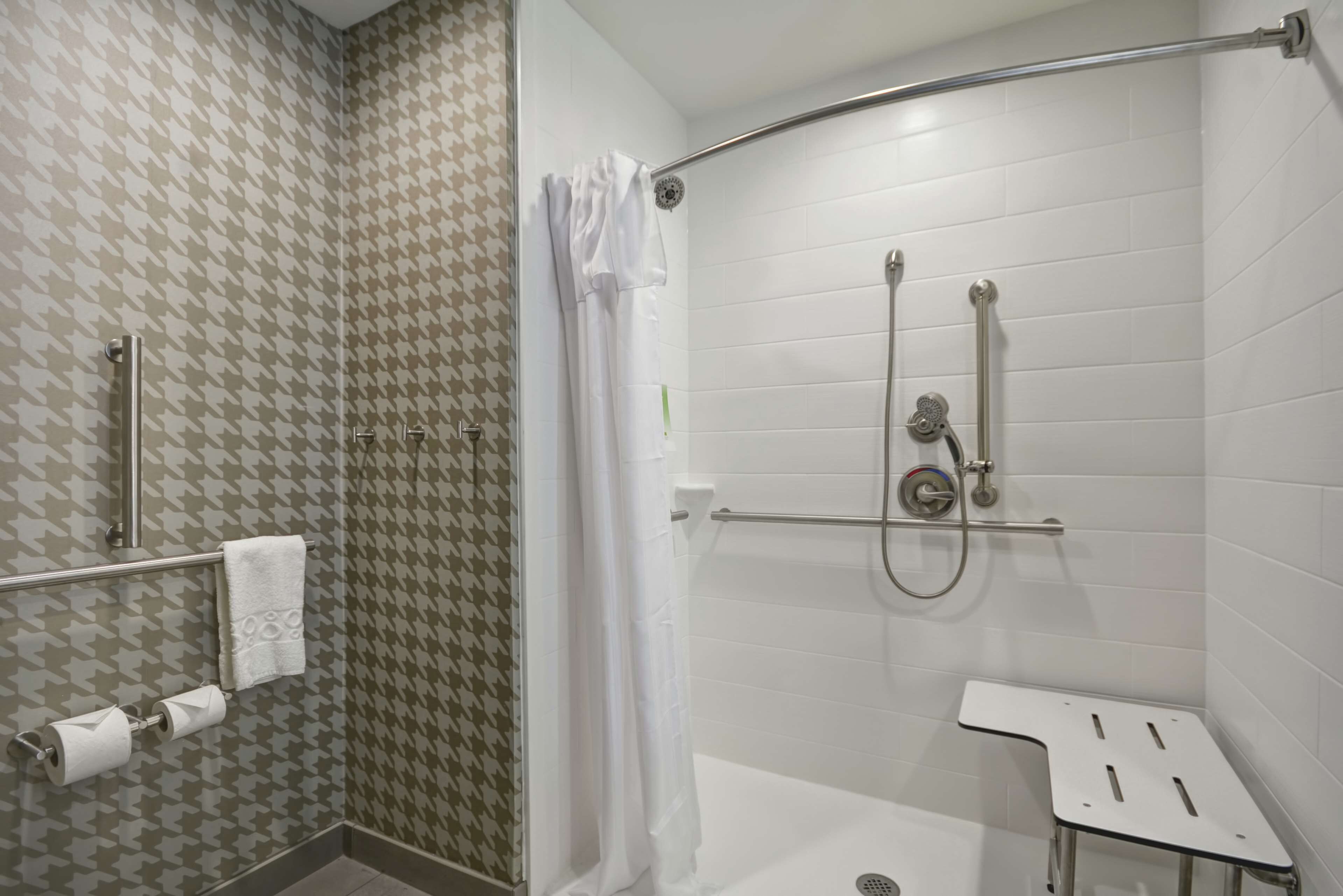 Un espacio de ducha con puerta de vidrio, una toalla blanca en un perchero y un panel de control de la ducha.