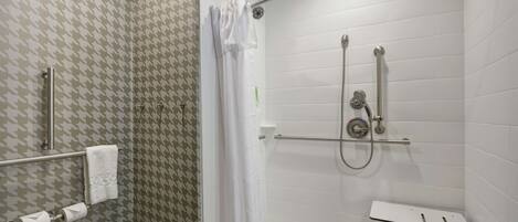 Un espacio de ducha con puerta de vidrio, una toalla blanca en un perchero y un panel de control de la ducha.
