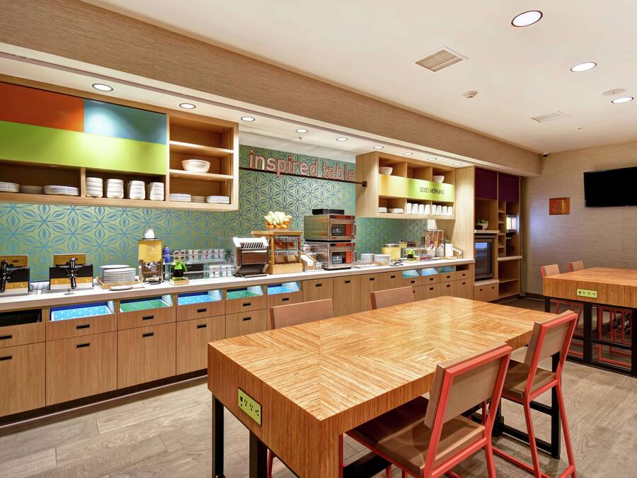 Un restaurante moderno con mesas y sillas de madera, una barra con productos alimenticios y un televisor montado en la pared.