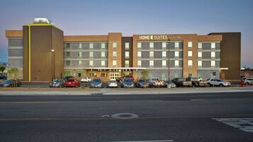 Un hotel de varios pisos con diseño moderno, destacando un letrero grande que dice 'Home 2 Suites by Hilton'.