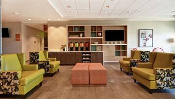 A modern hotel lobby with a reception desk, seating area, and a large TV screen.