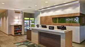 Un mostrador de recepción de hotel con un letrero que dice "HOME 2 Suites by Hilton" y una barra con un teléfono y una pantalla digital.