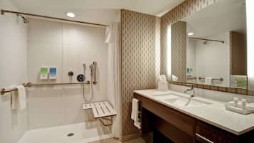 Un baño moderno con ducha a ras de suelo, un espejo grande y un tocador de madera.