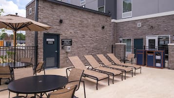 Un patio con sillones de descanso, una mesa redonda y un área de estar cubierta. Hay un letrero que indica llamar al 911 en caso de emergencia.