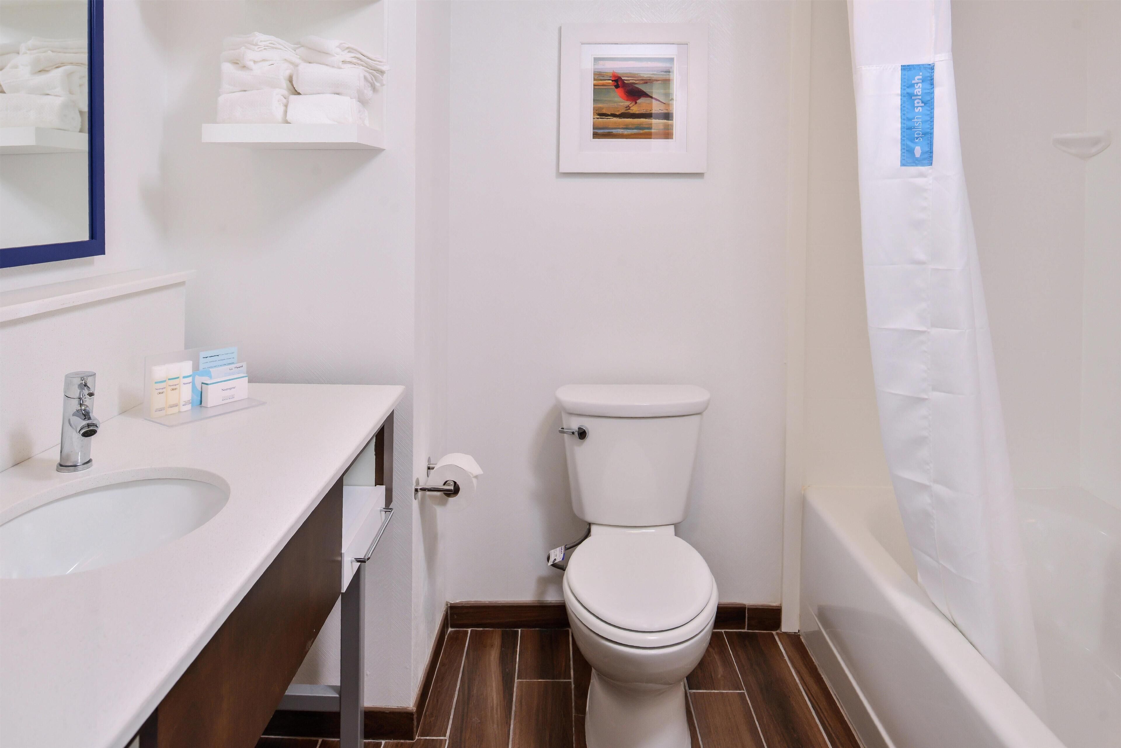 A bathroom with a white toilet, a sink with toiletries, and a framed picture on the wall.