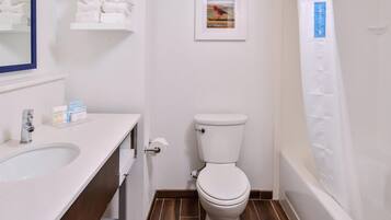 A bathroom with a white toilet, a sink with toiletries, and a framed picture on the wall.
