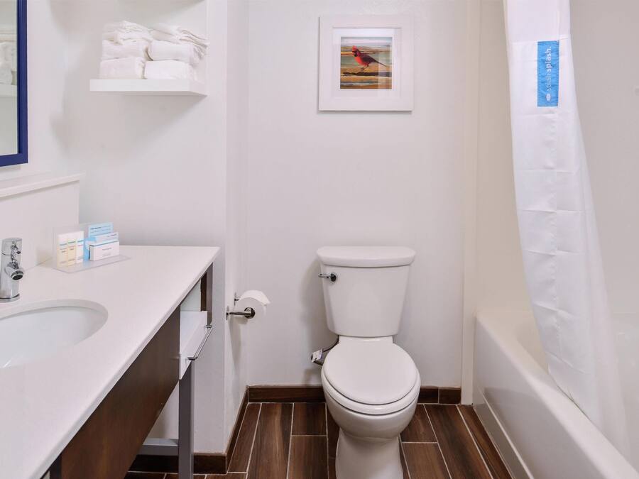 A bathroom with a white toilet, a sink with toiletries, and a framed picture on the wall.