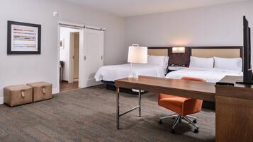 A hotel room with two beds, a desk, an orange chair, and a TV.