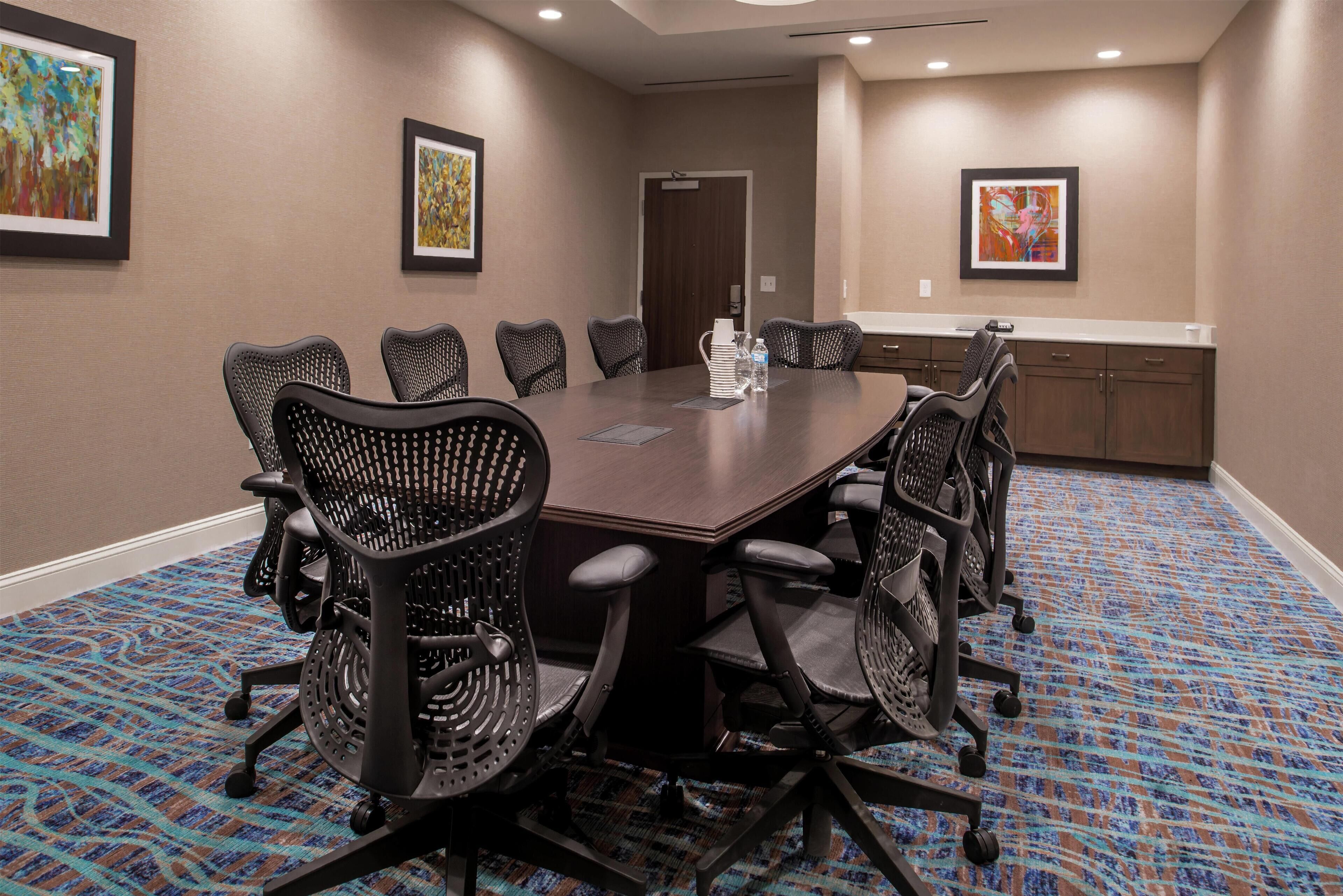 A conference room with a large table, six chairs, and a carpeted floor.