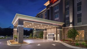 A Hampton Inn hotel entrance with a covered parking area, a well-lit facade, and a welcoming sign.