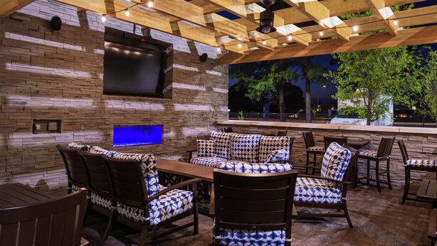 An outdoor patio with a stone wall, wooden ceiling, and seating area.