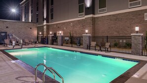 An indoor swimming pool with a brick wall, lounge chairs, and a metal pool ladder.