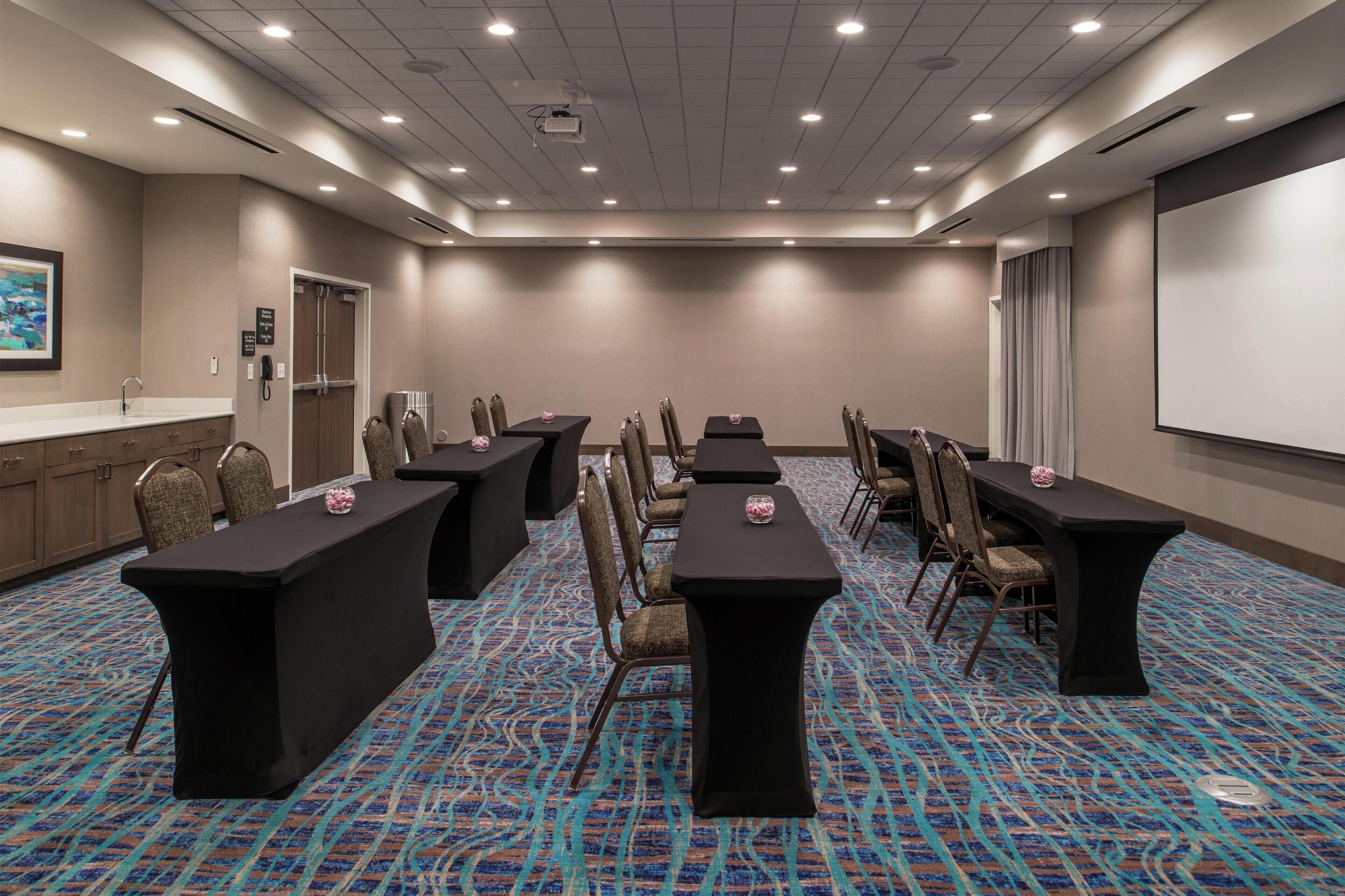 A conference room with a long table, chairs, a projector screen, and a carpeted floor.