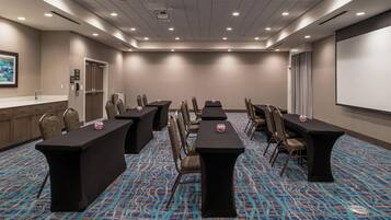 A conference room with a long table, chairs, a projector screen, and a carpeted floor.