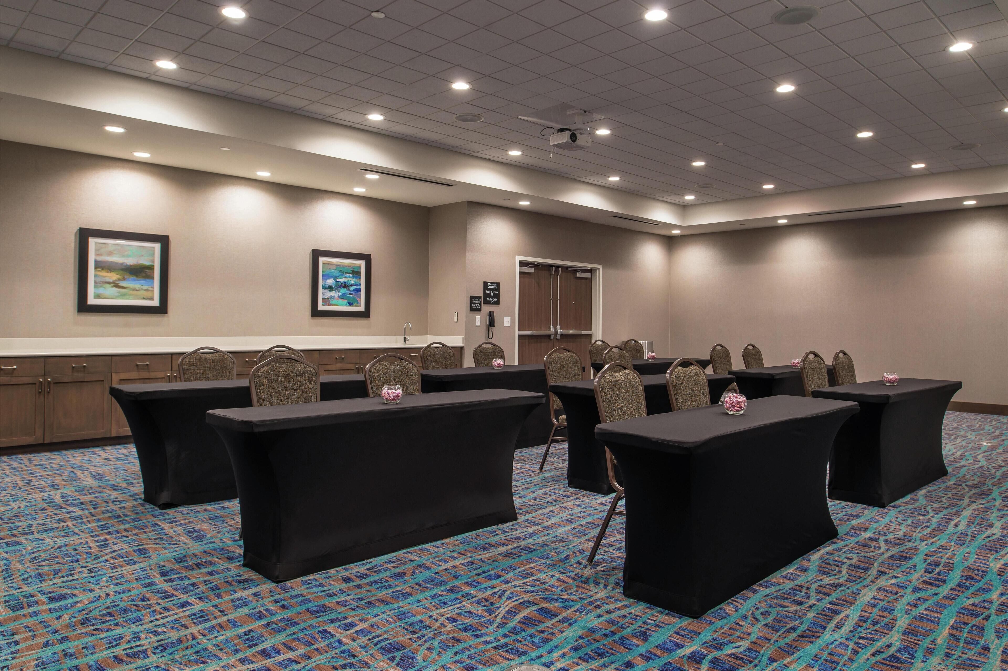 A conference room with tables and chairs, a projector, and framed pictures on the wall.